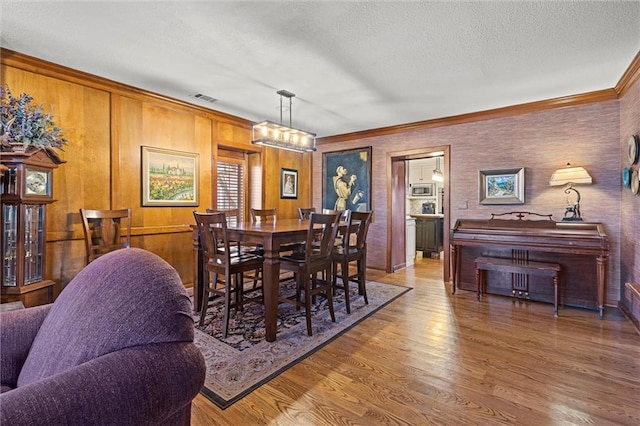 dining room featuring ornamental molding, wood finished floors, visible vents, and a textured ceiling