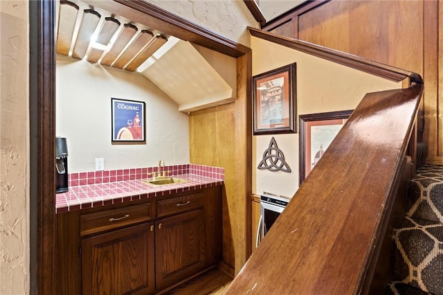 kitchen with dark brown cabinetry, tile countertops, a textured wall, and a sink