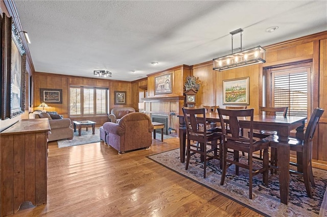 dining room featuring light wood-style floors, wood walls, a fireplace, and a textured ceiling