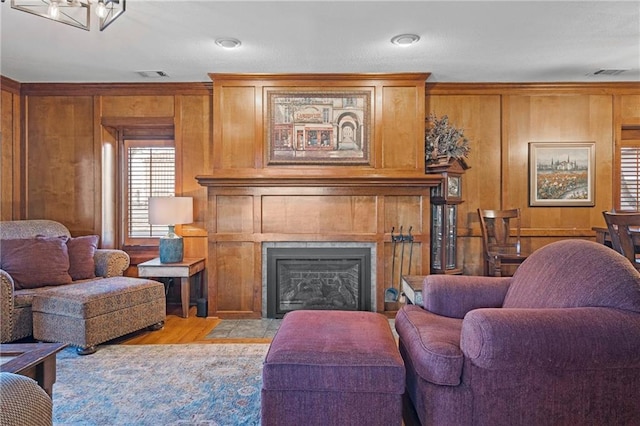 living area with light wood finished floors, wooden walls, a tile fireplace, and visible vents