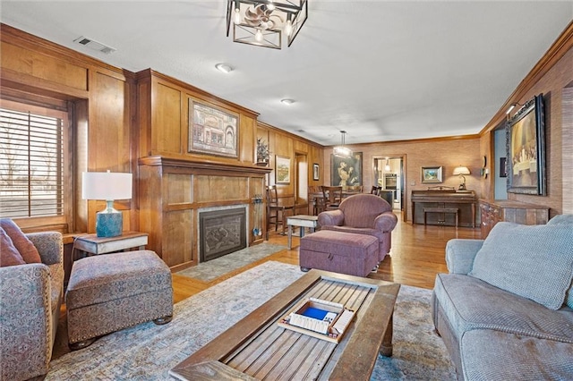 living room with visible vents, a fireplace with flush hearth, light wood-style floors, and crown molding