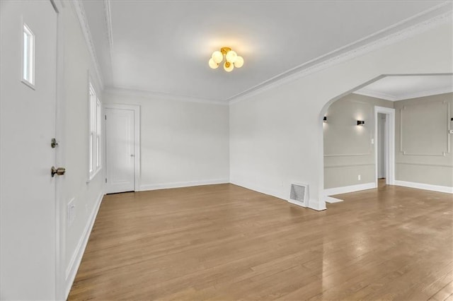 empty room featuring arched walkways, wood finished floors, visible vents, baseboards, and crown molding