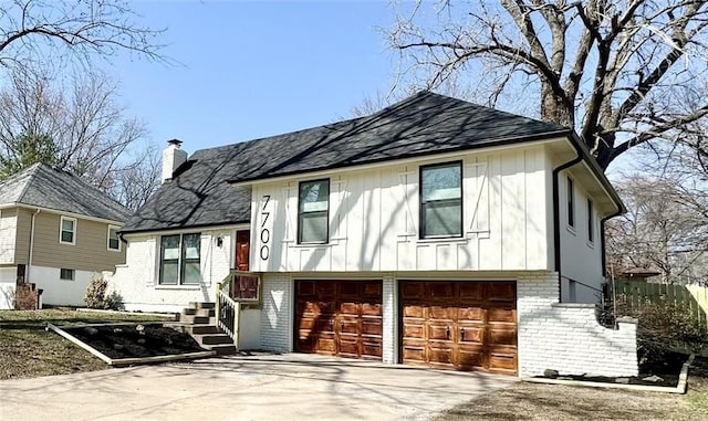 split level home with board and batten siding, concrete driveway, a garage, brick siding, and a chimney