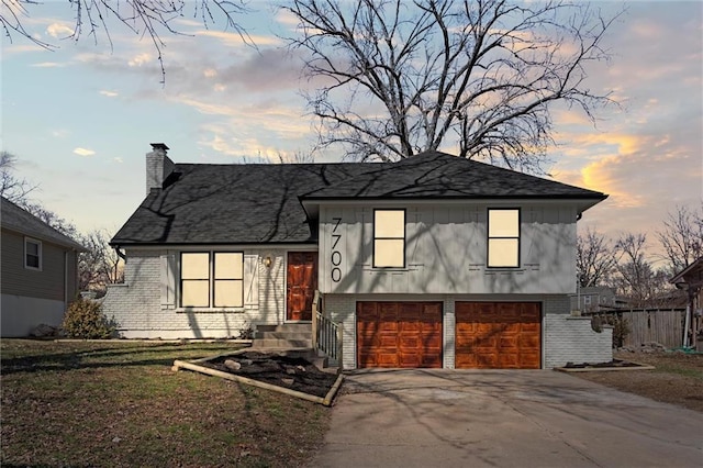 split level home featuring a garage, brick siding, driveway, and a chimney