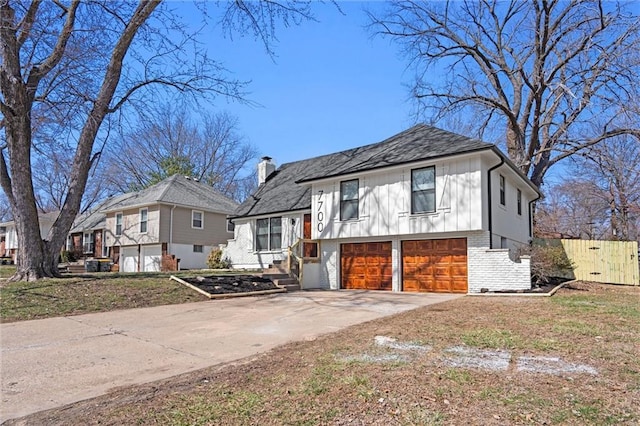 tri-level home featuring brick siding, a chimney, concrete driveway, a garage, and board and batten siding