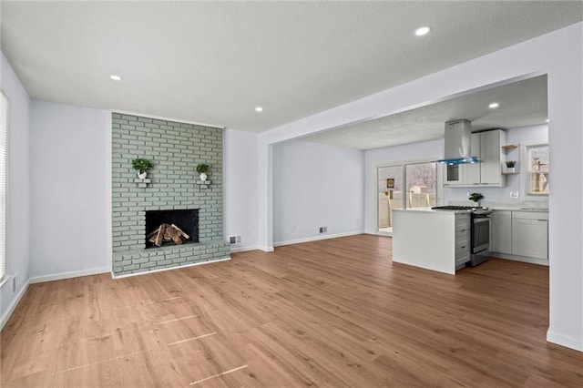 unfurnished living room featuring baseboards, recessed lighting, a fireplace, a textured ceiling, and light wood-type flooring