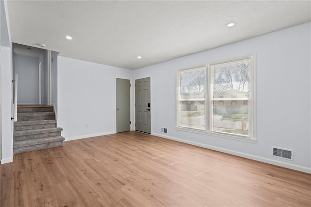 empty room featuring baseboards, visible vents, light wood finished floors, recessed lighting, and stairs