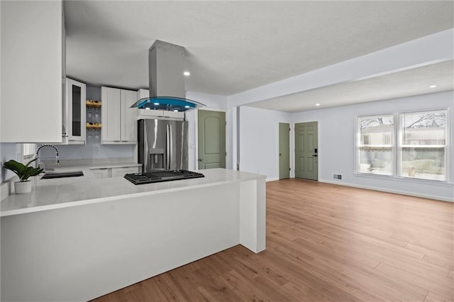 kitchen with light wood finished floors, light countertops, island exhaust hood, stainless steel refrigerator with ice dispenser, and a sink