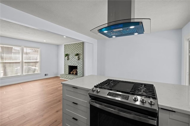 kitchen with gray cabinetry, light stone counters, a textured ceiling, light wood-style floors, and gas range