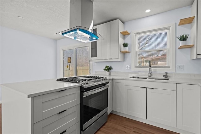 kitchen with open shelves, gas range, a peninsula, island exhaust hood, and a sink