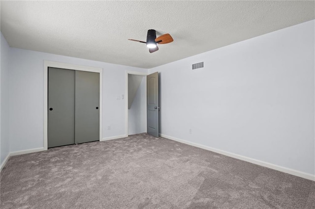 unfurnished bedroom with visible vents, a textured ceiling, a closet, carpet floors, and baseboards