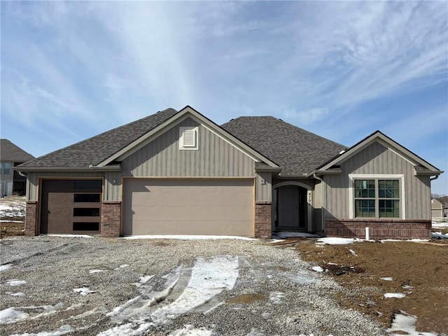 view of front of home with a garage, gravel driveway, brick siding, and roof with shingles