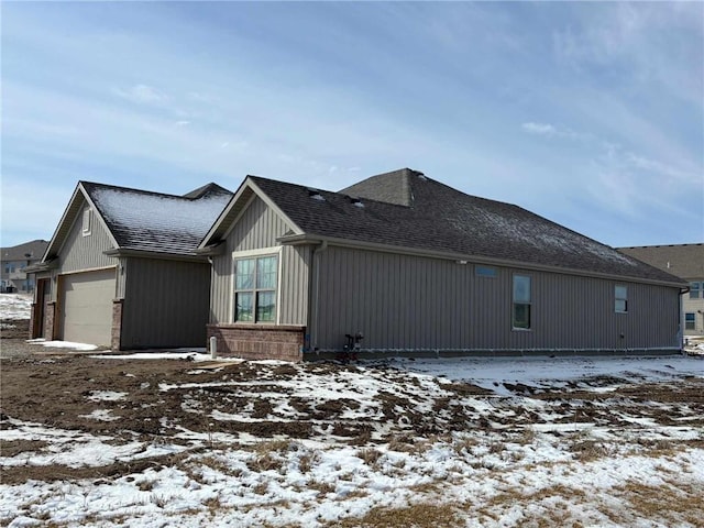 view of snowy exterior featuring a garage, brick siding, and a shingled roof