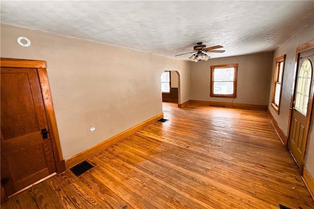 unfurnished room featuring baseboards, visible vents, arched walkways, wood finished floors, and a textured ceiling