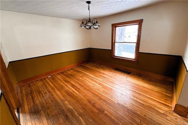 unfurnished room featuring hardwood / wood-style flooring, visible vents, and an inviting chandelier