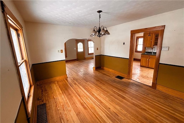 spare room featuring a chandelier, arched walkways, visible vents, and light wood finished floors