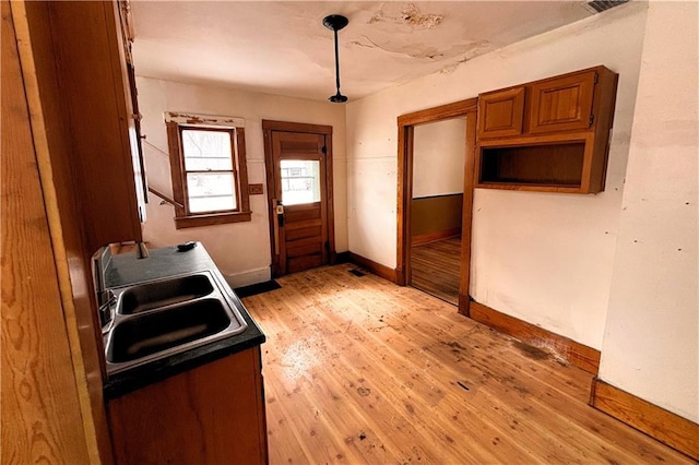 kitchen with light wood-style floors, brown cabinetry, a sink, and baseboards