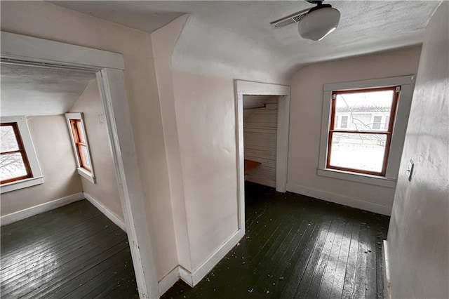 hallway with vaulted ceiling, wood-type flooring, visible vents, and baseboards