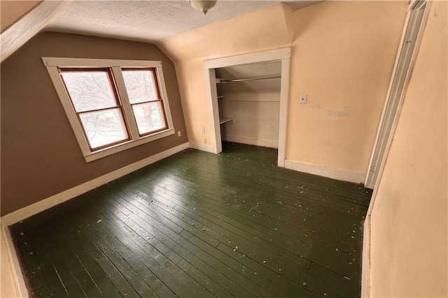 unfurnished bedroom featuring baseboards, lofted ceiling, dark wood-style flooring, a textured ceiling, and a closet