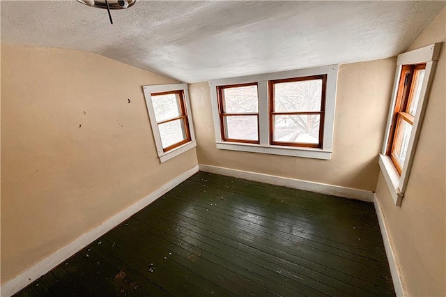 empty room with dark wood-type flooring, lofted ceiling, a textured ceiling, and baseboards