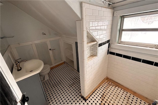 full bathroom with wainscoting, a tile shower, a sink, and toilet