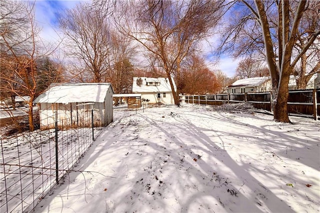 snowy yard with a storage unit, an outdoor structure, and a fenced backyard