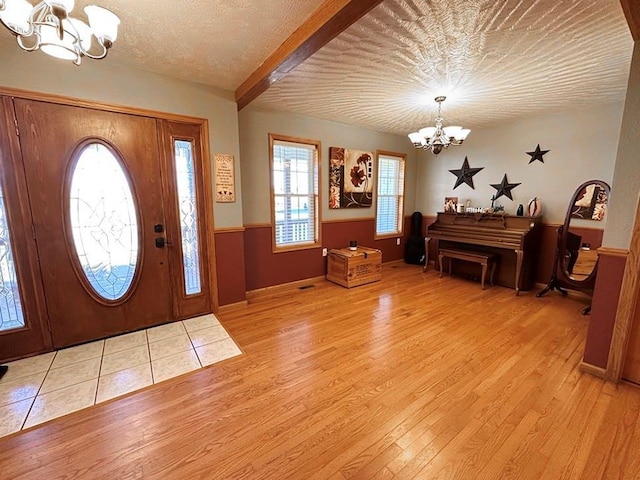 foyer entrance with light wood-style floors, wainscoting, a textured ceiling, and an inviting chandelier