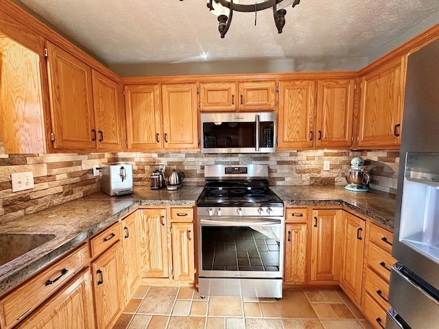 kitchen with a textured ceiling, stainless steel appliances, dark stone countertops, and backsplash