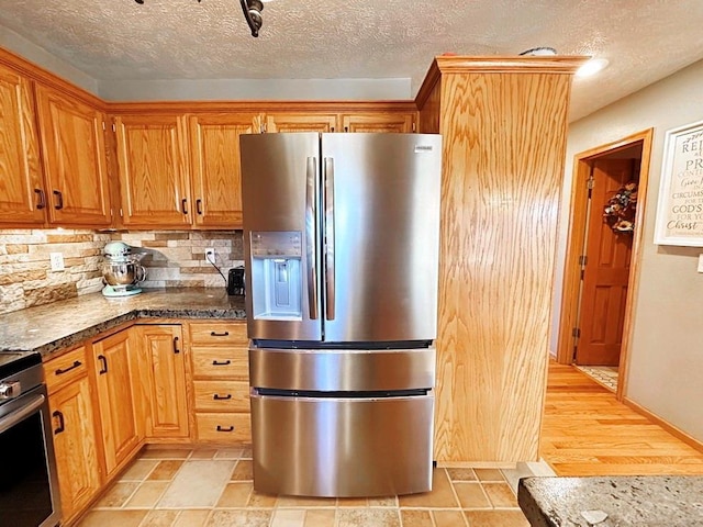 kitchen with brown cabinets, stainless steel appliances, tasteful backsplash, a textured ceiling, and dark stone countertops