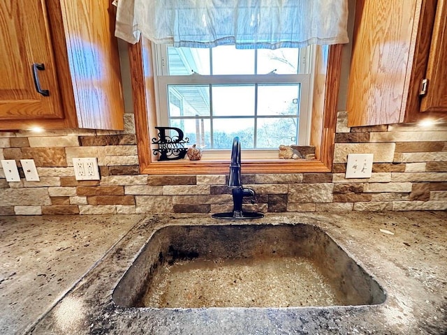 kitchen featuring brown cabinets, stone countertops, a sink, and decorative backsplash