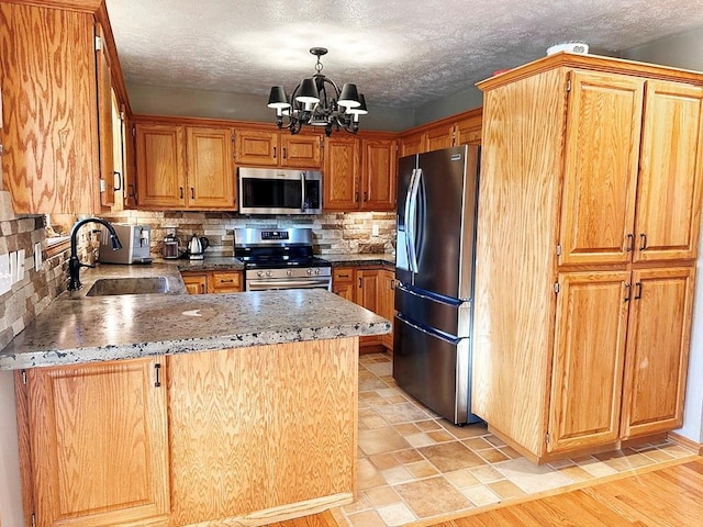 kitchen featuring a notable chandelier, stainless steel appliances, backsplash, a sink, and a peninsula