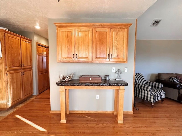 kitchen featuring light wood-type flooring, visible vents, open floor plan, and a textured ceiling