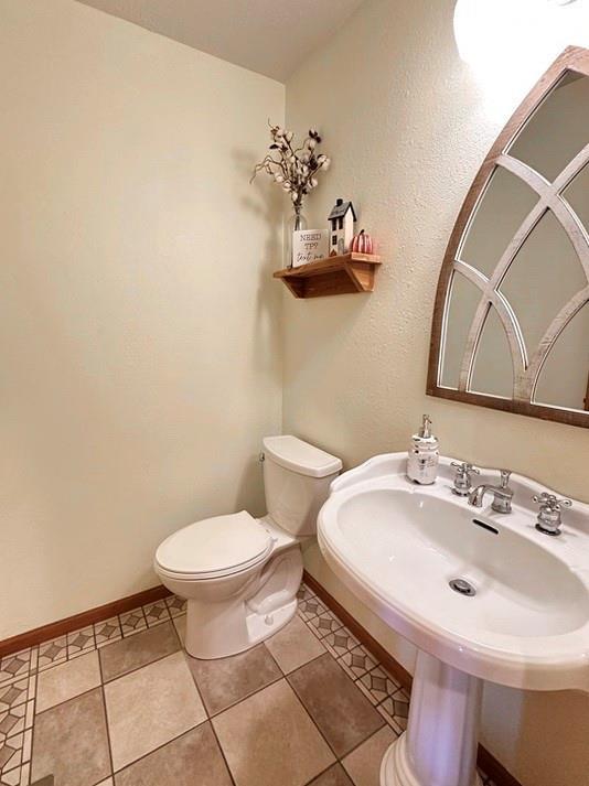 half bathroom with toilet, tile patterned flooring, baseboards, and a sink