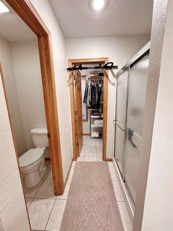 full bath featuring a textured ceiling, toilet, a spacious closet, a shower stall, and tile patterned floors