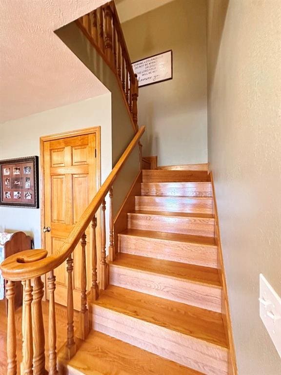 stairway with a textured wall, baseboards, a textured ceiling, and wood finished floors