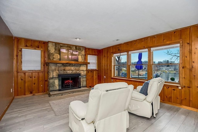 living room featuring light wood finished floors, a fireplace, visible vents, and wooden walls