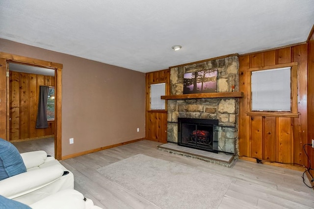 living area with light wood-style floors, a fireplace, wooden walls, and baseboards