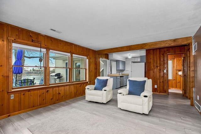 sitting room with visible vents, wood walls, light wood-style flooring, and baseboards