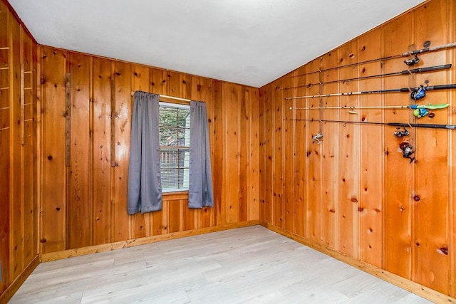 unfurnished room featuring vaulted ceiling, wooden walls, baseboards, and wood finished floors