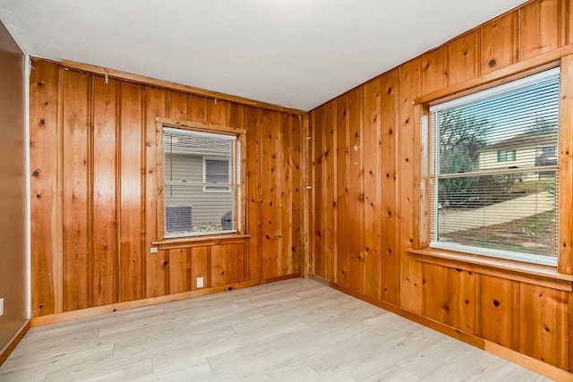 empty room with light wood-type flooring, wood walls, and baseboards