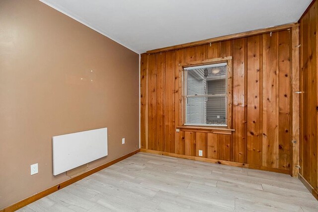 unfurnished room featuring light wood-type flooring, wood walls, and baseboards