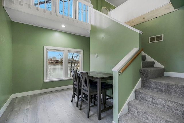 staircase featuring baseboards, visible vents, a high ceiling, and wood finished floors