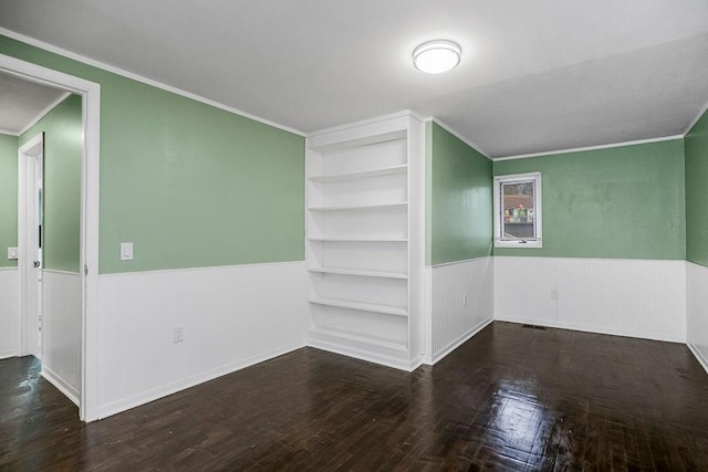 empty room with built in features, a wainscoted wall, crown molding, visible vents, and wood finished floors