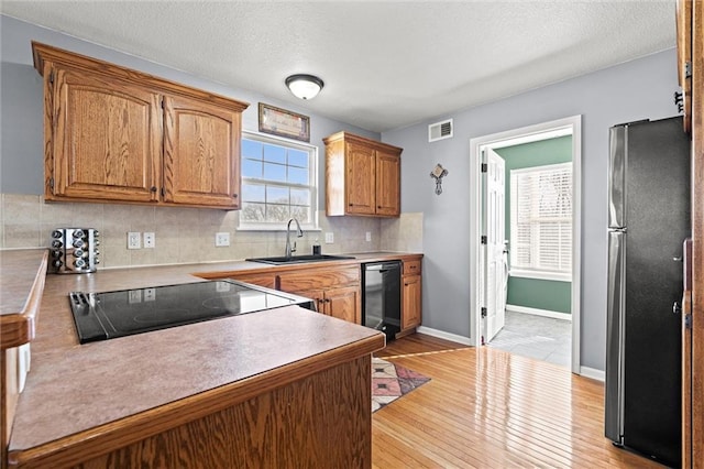 kitchen with visible vents, light wood-type flooring, a sink, freestanding refrigerator, and decorative backsplash