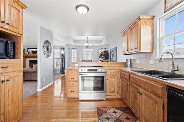 kitchen with a tray ceiling, a peninsula, light wood-style floors, black appliances, and a sink