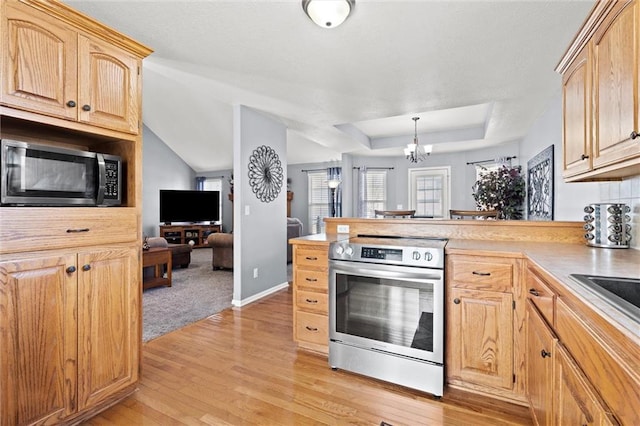 kitchen with light wood-type flooring, a peninsula, an inviting chandelier, stainless steel appliances, and a raised ceiling