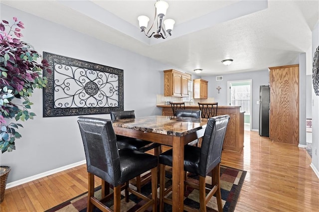 dining space featuring a tray ceiling, baseboards, a notable chandelier, and light wood finished floors