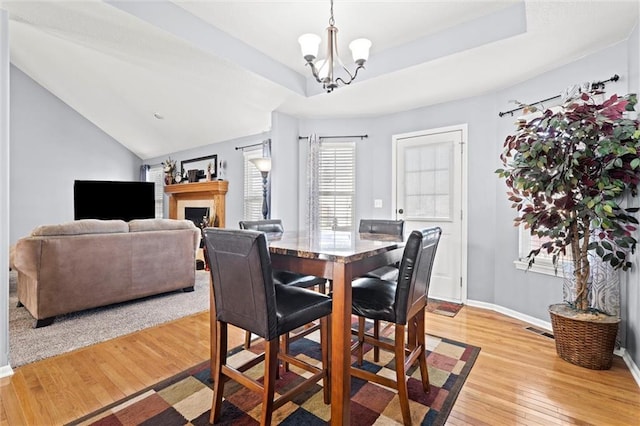 dining space with baseboards, light wood finished floors, an inviting chandelier, a fireplace, and a raised ceiling