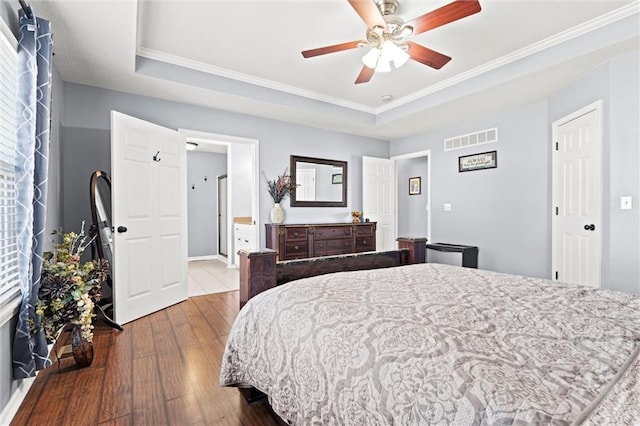 bedroom with visible vents, ornamental molding, wood finished floors, a raised ceiling, and ceiling fan