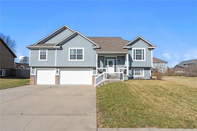 split foyer home featuring a front yard, covered porch, concrete driveway, a garage, and brick siding